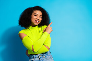 Smiling young woman in a neon green top standing against a bright blue background, showcasing an inviting pose and positive attitude.