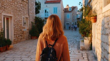 Fototapeta premium Young woman walking down a charming cobblestone street in a historic village during golden hour sunset
