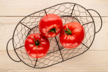 Three pink tomatoes in a basket on a wooden table, close-up, top view.