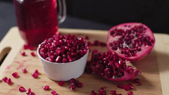Ceramic bowl full of pomegranate and cutted pomegranate with seeds lie on a wooden cutting board on the concrete background