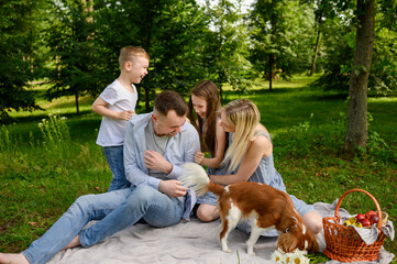Happy family relaxing in park sitting on blanket with dogs. Boy, girl and mom tickling dad having...