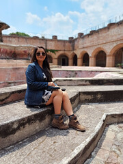 Mujer latina bonita, sentada en una fuente antigua construida hace cientos de años, viaje por...