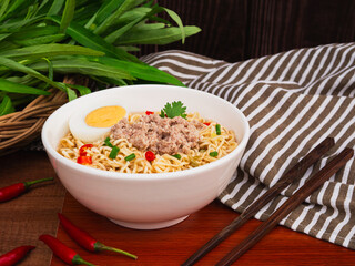 Instant noodle soup with minced pork and half boiled egg in white bowl on wooden table background. Asia Food