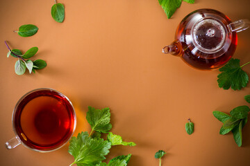 Green tea with currant leaves and mint in glass teapot and cup on brown background. Top view