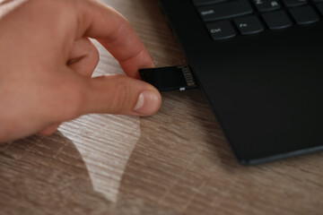 Man inserting SD memory card into laptop at wooden table, closeup