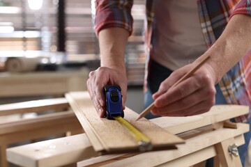 Man measuring wooden plank with tape and pencil indoors, closeup