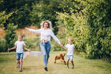 Fototapeta premium Mother and sons flying a kite. Happy Family day. Family flying a kite in a clearing near the forest.