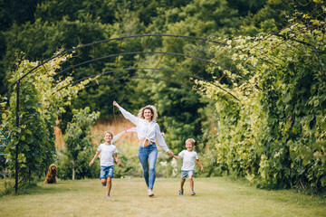 Obraz premium Mother and sons flying a kite. Happy Family day. Family flying a kite in a clearing near the forest.