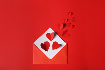 Paper hearts flying out of envelope on red background, flat lay