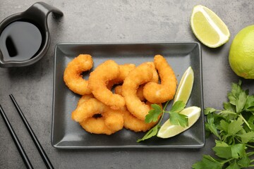 Tasty tempura shrimps, lime, parsley and soy sauce on grey textured table, flat lay