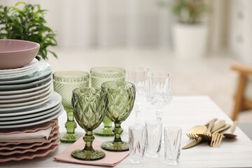 Clean glasses, plates, cutlery and green houseplant on white wooden table indoors
