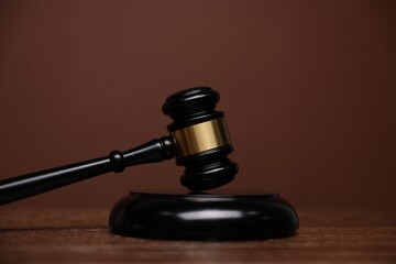 Judge's gavel and sound block on wooden table against brown background, closeup