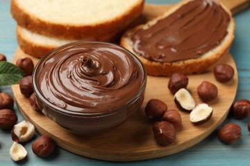 Chocolate hazelnut spread in bowl, nuts and toasts on light blue wooden table, closeup