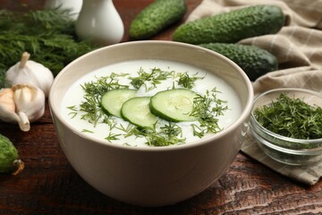 Tasty cucumber soup in bowl and ingredients on wooden table, closeup