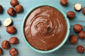 Tasty chocolate hazelnut spread and nuts on blue wooden table, flat lay