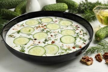 Fresh tasty cucumber soup and ingredients on white table, closeup