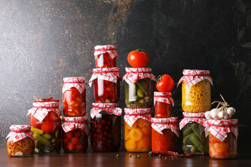 Many jars with different pickled products and ingredients on wooden table