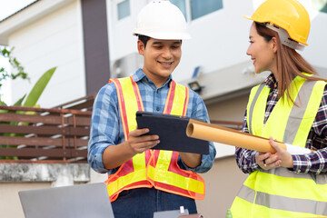 Male and female engineers wearing hard hats smile and discuss blueprints on a construction site, demonstrating teamwork, safety and expertise.