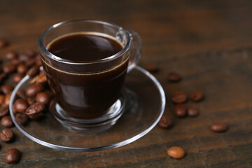 Aromatic coffee in glass cup and beans on wooden table, closeup. Space for text