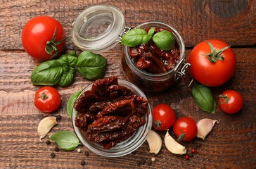 Delicious sun dried tomatoes in glass dishware, fresh vegetables and spices on wooden table, flat lay