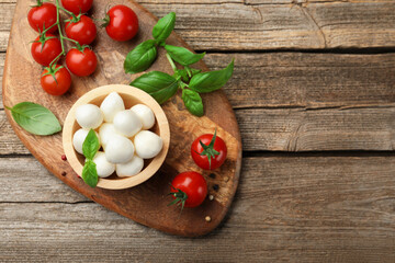 Tasty mozzarella cheese balls in bowl, basil, peppercorns and tomatoes on wooden table, top view. Space for text