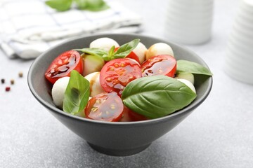 Tasty salad with mozzarella, tomatoes and basil on light table, closeup