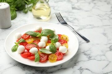 Tasty salad with mozzarella, tomatoes and basil served on white marble table