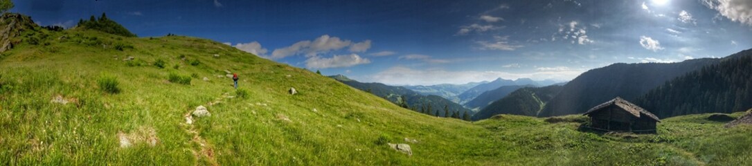 Panoramic view of a mountain meadow with wooden cabin under sunny skies