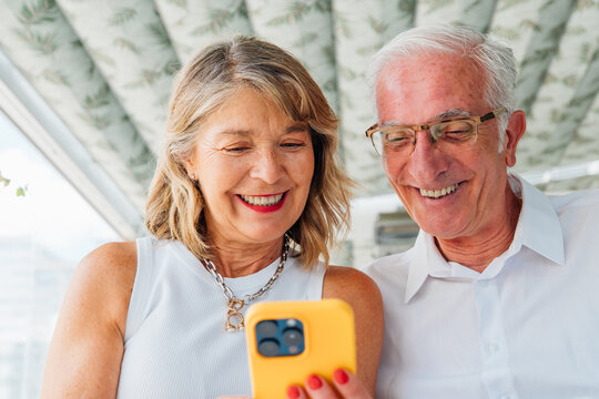 Mature couple sharing smartphone moment, connecting through technology while lovingly interacting, representing active senior lifestyle and digital engagement - Powered by Adobe
