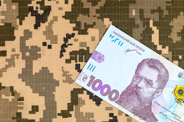 Ukrainian hryvnia on the background of pixel camouflage uniforms of the Ukrainian army. War in...