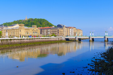 Along the coast of the city of Donostia, the Urumea River passes under the elegant structure of the Kursaal Bridge, reflecting light on the buildings that line its banks.