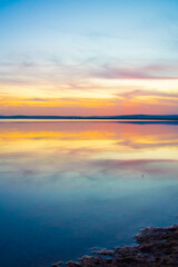Colorful sunset reflecting on a calm lake surface. Vivid tones of purple, yellow, and blue create a magical and serene atmosphere.