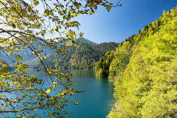 Beautiful view through tree branches on the famous lake Ritsa in the mountains of Abkhazia on a warm sunny day. Autumn warm day