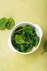 Freshly steamed spinach leaves in a white bowl, resting on a green backdrop, promoting healthy eating and vegetarian lifestyles