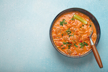 Delicious brazilian moqueca de camarao with shrimps, peppers, lime, and cilantro served in a bowl, garnished with parsley and served in a rustic bowl on light blue background, copy space
