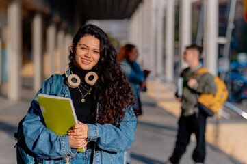 Smiling female university student holding notebooks, enjoying her return to school while embracing...