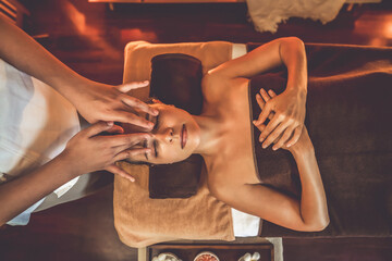 Fototapeta premium Caucasian woman enjoying relaxing anti-stress head massage and pampering facial beauty skin recreation leisure in warm candle lighting ambient salon spa in luxury resort or hotel. Quiescent