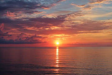 Fototapeta premium Fiery Sunset with Orange Clouds Reflecting on Calm Sea Waters, Nature's Serenity