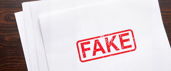 Stack of documents labeled FAKE on office desk, highlighting deception