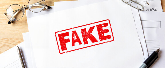 Red FAKE stamp on documents in simple workspace, document authenticity