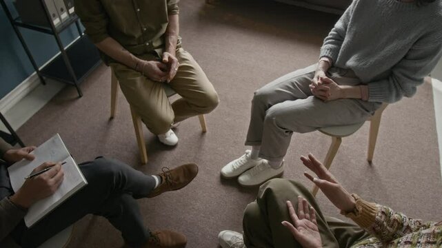 Cropped shot of group therapy session in progress, showing participants seated in circle with open body language, sharing thoughts in confidential setting
