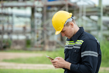 Engineer or refinery worker using mobile phone, texing or searching data while taking a break at...