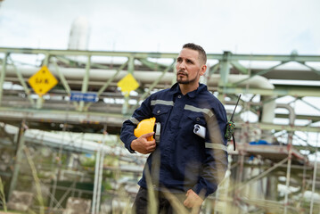 Surveyor or refinery worker in safety gear holding hardhat inspecting at oil petroleum factory....