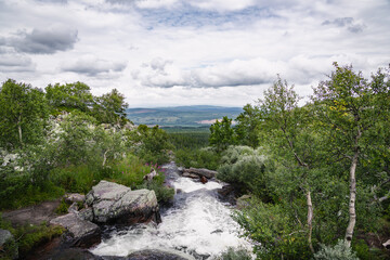 Njupån river cascades over rocks, forming a waterfall as it flows through Fulufjället National Park in Dalarna, Sweden, surrounded by lush greenery and vast landscape