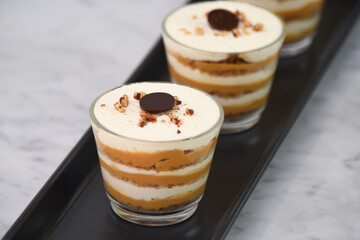 classic Tiramisu Dessert in clear glasses showcasing layers of coffee soaked, creamy mascarpone, and dusted cocoa topped with whipped cream, and chopped nuts closeup view of Italian dessert