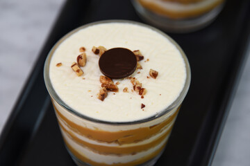 classic Tiramisu Dessert in clear glasses showcasing layers of coffee soaked, creamy mascarpone, and dusted cocoa topped with whipped cream, and chopped nuts closeup top view of Italian dessert