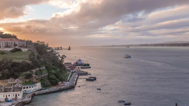 Aerial timelapse panorama from a hill near Porto Brandao Ferry Station on the Tagus River in Lisbon. Dramatic sunset with colorful clouds, a ship floating on water and Terminal in background