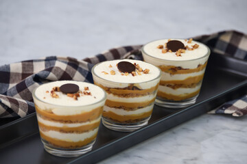 classic Tiramisu Dessert in clear glasses with napkin showcasing layers of coffee soaked, creamy mascarpone, and dusted cocoa topped with whipped cream, and chopped nuts side view of Italian dessert