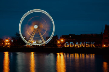 Gdansk Poland Ferris wheel in the old town of Gdansk at night evening dusk Reflection in river water Europe. Long exposure photo. City scenic view Illuminated attraction park and street with beautiful