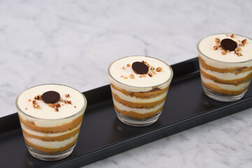 classic Tiramisu Dessert in clear glasses showcasing layers of coffee soaked, creamy mascarpone, and dusted cocoa topped with whipped cream, and chopped nuts closeup side view of Italian dessert